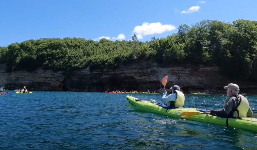 Two guys kayaking in a long green kayak on a lake